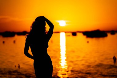 Güzel, çıplak bir Latin model, egzotik bir Karayip plajında güneşin doğuşuyla poz verirken siluete bürünür.