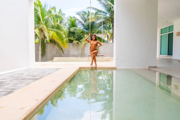 A beautiful brunette nude model swings by the pool in the Yucatan Peninsula near Merida, Mexico