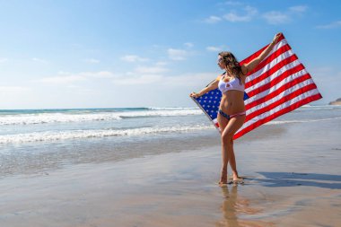 Muhteşem bir esmer manken kumsalda Amerikan bayrağıyla poz veriyor. 