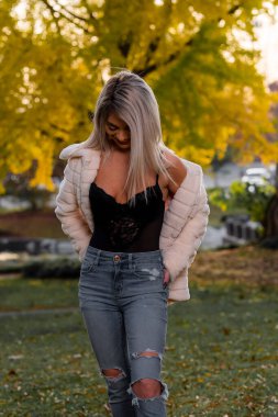 Genç ve güzel bir sarışın model, bir sonbahar gününün tadını çıkarırken dışarıda poz veriyor.