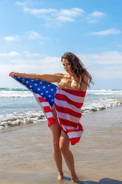Muhteşem bir esmer model, kumsalda Amerikan bayrağıyla çıplak poz veriyor. 