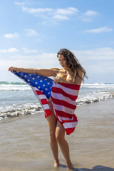 Muhteşem bir esmer model, kumsalda Amerikan bayrağıyla çıplak poz veriyor. 