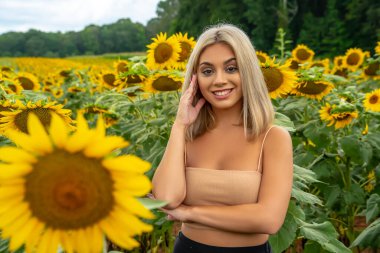 Sarışın bir model, yaz gününün tadını çıkarırken ayçiçeği tarlasında poz veriyor.