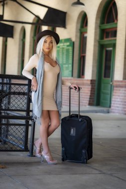 Sarışın bir model tren istasyonunda tren beklerken dışarıda poz veriyor.