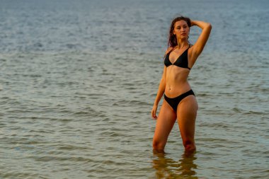 Güzel bir esmer bikini mankeni sahilde açık havanın tadını çıkarır.