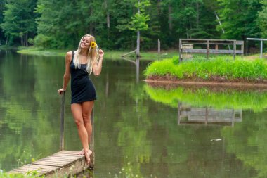 Muhteşem sarışın bir manken, yaz gününün tadını çıkarırken göletin kenarında poz veriyor.