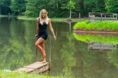 Muhteşem sarışın bir manken, yaz gününün tadını çıkarırken göletin kenarında poz veriyor.