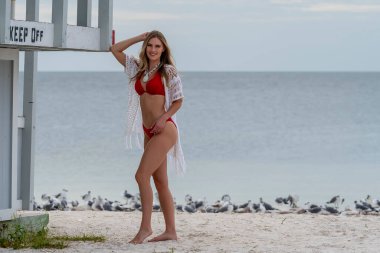 Güzel sarışın bir bikini mankeni bir cankurtaran istasyonunun yanında poz verirken sahilde havanın tadını çıkarıyor.