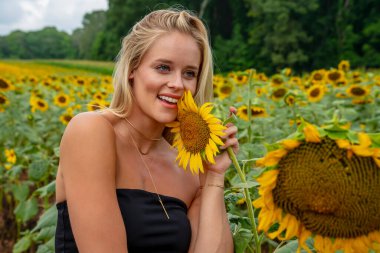 Sarışın bir model, yaz gününün tadını çıkarırken ayçiçeği tarlasında poz veriyor.