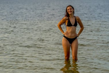 Güzel bir esmer bikini mankeni sahilde açık havanın tadını çıkarır.