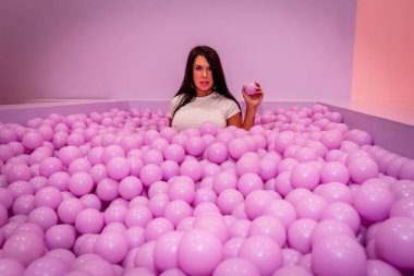 Güzel bir Asyalı model büyük miktarda plastik toplarla renkli bir odada oynar.