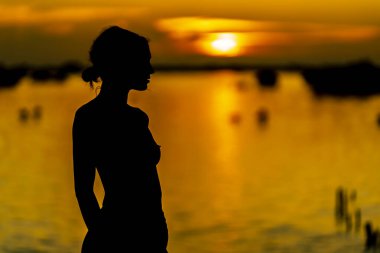 Güzel, çıplak bir Latin model, egzotik bir Karayip plajında güneşin doğuşuyla poz verirken siluete bürünür.