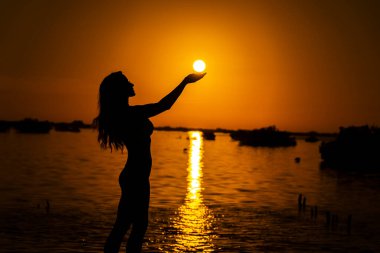 Güzel, çıplak bir Latin model, egzotik bir Karayip plajında güneşin doğuşuyla poz verirken siluete bürünür.