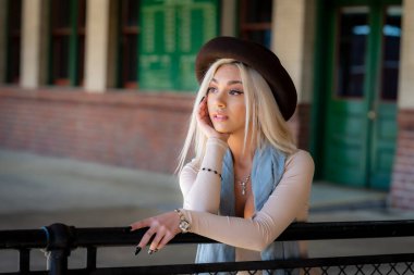 Sarışın bir model tren istasyonunda tren beklerken dışarıda poz veriyor.