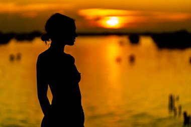 Güzel, çıplak bir Latin model, egzotik bir Karayip plajında güneşin doğuşuyla poz verirken siluete bürünür.