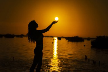 Güzel, çıplak bir Latin model, egzotik bir Karayip plajında güneşin doğuşuyla poz verirken siluete bürünür.