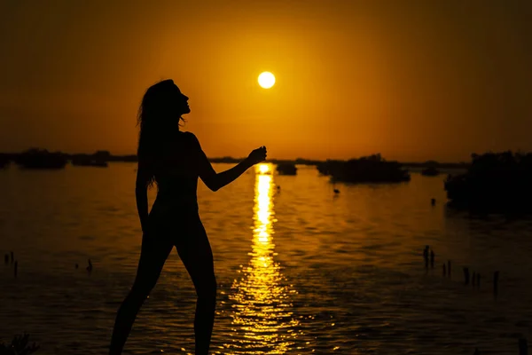 A beautiful nude latin model is silhouetted as she poses with the rising sun behind her on a exotic Caribbean beach