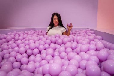 Güzel bir Asyalı model büyük miktarda plastik toplarla renkli bir odada oynar.