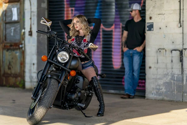 Sarışın bir model şehir ortamında motosikletiyle dışarıda poz veriyor.