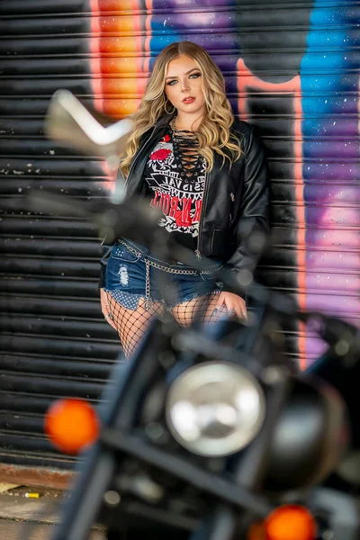 Sarışın bir model şehir ortamında motosikletiyle dışarıda poz veriyor.