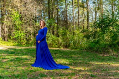 Güzel, hamile bir anne açık havada poz verir.