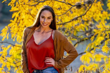 Muhteşem bir esmer model, sonbahar havasının tadını çıkarırken dışarıda poz veriyor.