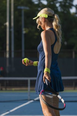 Sarışın bir model tenis kortunda öğleden sonra güneşinde tenis oynuyor.