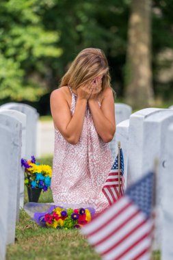 A young bride shows her grief at the burial site of a family member at a military cemetery clipart