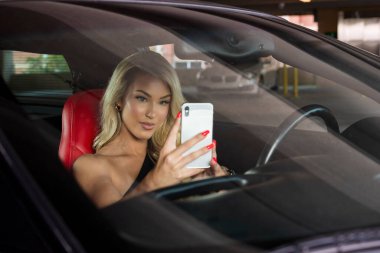 Güzel sarışın bir manken spor arabasını sürmeden önce cep telefonuyla konuşur.