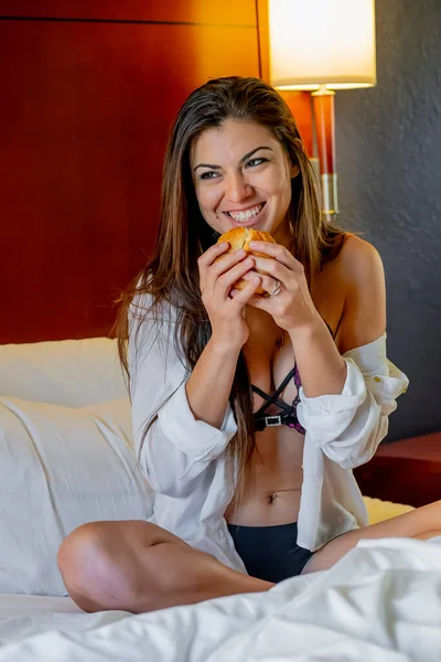 ベッドルーム環境でベッドで朝食を食べながら美しいヒスパニック系の女性がランジェリーにポーズ — ストック写真