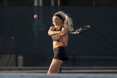 Sarışın bir model tenis kortunda öğleden sonra güneşinde tenis oynuyor.