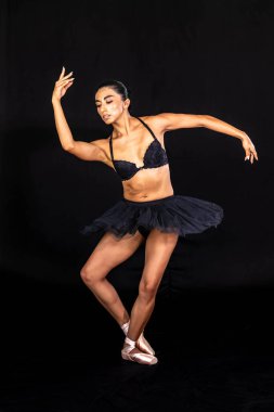 Göz kamaştırıcı bir balerin, loş bir stüdyoda zarif bir poz verir, dramatik gölgeler onun kusursuz şeklini ve büyüleyici zarafetiyle zamansız duruşunu izler..