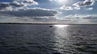 Mavi gökyüzünün altında, sakin liman sularında süzülen küçük bir su aracının hava aracı görüntüsü, güneş batarken ve ılık altın ışık huzur sahnesine hafifçe yansıyor..