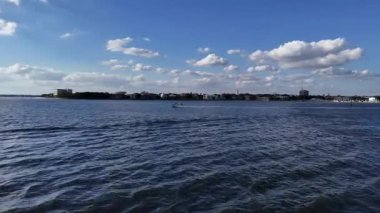 Mavi gökyüzünün altında, sakin liman sularında süzülen küçük bir su aracının hava aracı görüntüsü, güneş batarken ve ılık altın ışık huzur sahnesine hafifçe yansıyor..