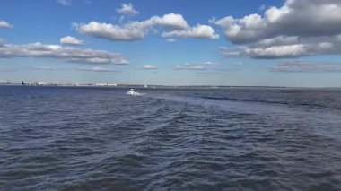 Mavi gökyüzünün altında, sakin liman sularında süzülen küçük bir su aracının hava aracı görüntüsü, güneş batarken ve ılık altın ışık huzur sahnesine hafifçe yansıyor..