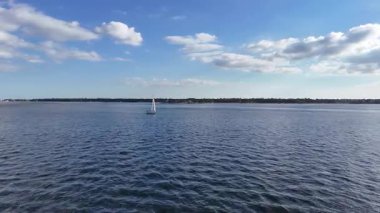 Mavi gökyüzünün altında, sakin liman sularında süzülen küçük bir su aracının hava aracı görüntüsü, güneş batarken ve ılık altın ışık huzur sahnesine hafifçe yansıyor..