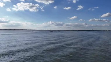 Mavi gökyüzünün altında, sakin liman sularında süzülen küçük bir su aracının hava aracı görüntüsü, güneş batarken ve ılık altın ışık huzur sahnesine hafifçe yansıyor..