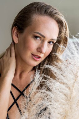 Güzel bir Doğu Avrupalı iç çamaşırı modeli beyaz bir yatakta, doğal pencere ışığıyla hafifçe aydınlatılarak samimi, sakin ve sıcak bir ev atmosferi yaratıyor..