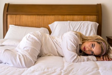 Narin dantelli iç çamaşırlı çarpıcı bir sarışın yumuşak ışıklı yatak odasında uzanır, gözleri heyecandan parlar. Sıcak bir parıltı onu zarafet ve cazibe havasıyla saran romantik ve samimi atmosferi güçlendirir..