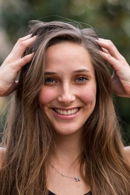 Genç ve güzel bir kadın bahar havasında zarif bir şekilde parkta yürüyor. Etrafı çiçeklerle ve yumuşak günışığıyla çevrili, günün sakin ve huzurlu ritminin tadını çıkarıyor..