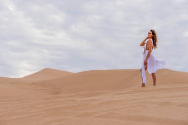 Zarif model kum tepelerindeki doğanın güzelliğini kucaklıyor, engin, doğal ihtişamın arkaplanına karşı zarafeti simgeliyor.