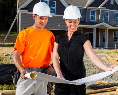 Güneşli bir inşaat sahasında, bir inşaat işçisi ve bir mühendis birlikte planları inceliyor, çizgileri ölçüyor ve ayrıntıları tartışıyor çerçeveler yükselirken, takım çalışması güvenli bir aile evini şekillendiriyor..