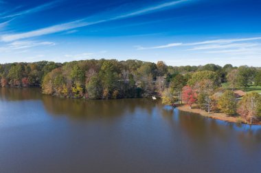 Nefes kesici bir sonbahar sahnesi: parlak mavi bir göl altında parlak bir mavi gökyüzünün altında süzülen renkli yapraklar, mükemmel bir sonbahar gününün canlı ve canlı güzelliğini yansıtıyor. Güneşler güzel bir sonbahar öğleden sonrasında bir gölün üzerinde batıyor.