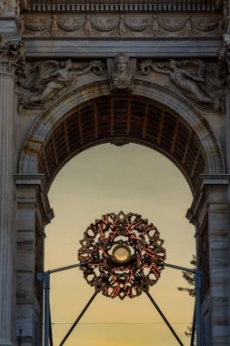 Milan 'daki Arco della Pace' in altında, Olimpiyat kazanı kemerin kalbinde parlıyor, parlak alev birliği, kutlamayı ve Oyunların ruhunu sembolize ederken kalabalıkları çekiyor..