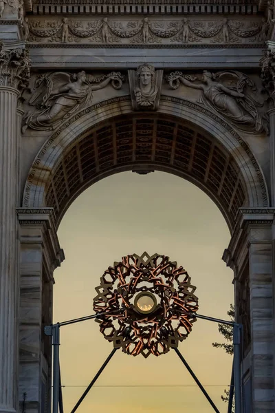 Milan 'daki Arco della Pace' in altında, Olimpiyat kazanı kemerin kalbinde parlıyor, parlak alev birliği, kutlamayı ve Oyunların ruhunu sembolize ederken kalabalıkları çekiyor..