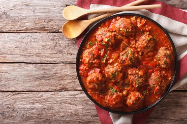 Masanın üzerinde bir tabakta baharatlı domates soslu köfte. Yatay
