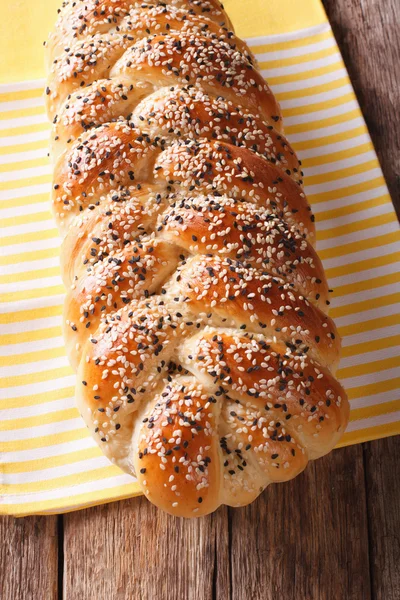 Delicioso bollo trenzado con semillas de sésamo en primer plano sobre la mesa. vertical — Foto de Stock