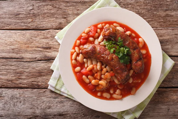 Grilled sausage with beans in tomato sauce on a plate close-up.