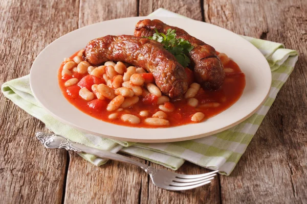 Pork sausages with beans and cooked tomatoes on a plate close-up