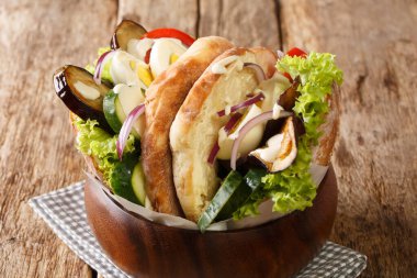 Bir sabich tarifi Orta Doğu sandviçi kızarmış patlıcan, haşlanmış yumurta, humus ve masada yakın plan diğer sebzeler içerir. Yatay